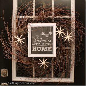 Learn How to MAKE a beautiful DIY Winter Wreath! See this easy winter wreath tutorial and the supply list. This rustic twiggy wreath features a framed winter printable and DIY fluffy white yarn snowflakes to add a cozy touch to your front door!