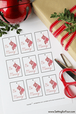 Free Printable Christmas Gift Tags with a holiday present wrapped in simple kraft paper, red ribbon with a red jingle bells and boxwood stems.