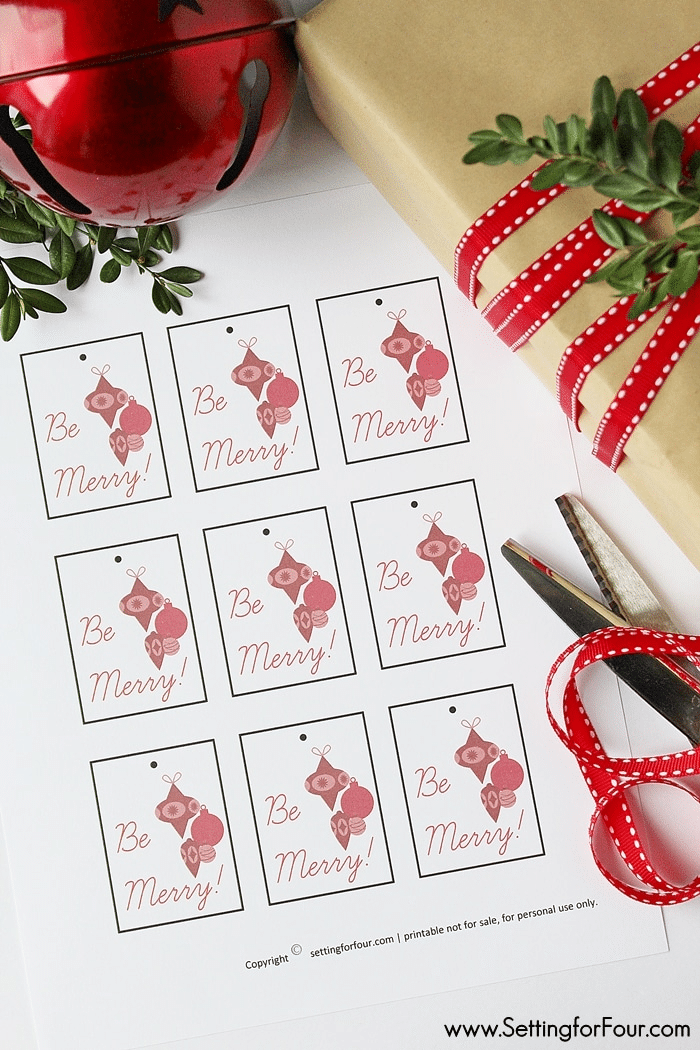Free Printable Christmas Gift Tags with a holiday present wrapped in simple kraft paper, red ribbon with a red jingle bells and boxwood stems.