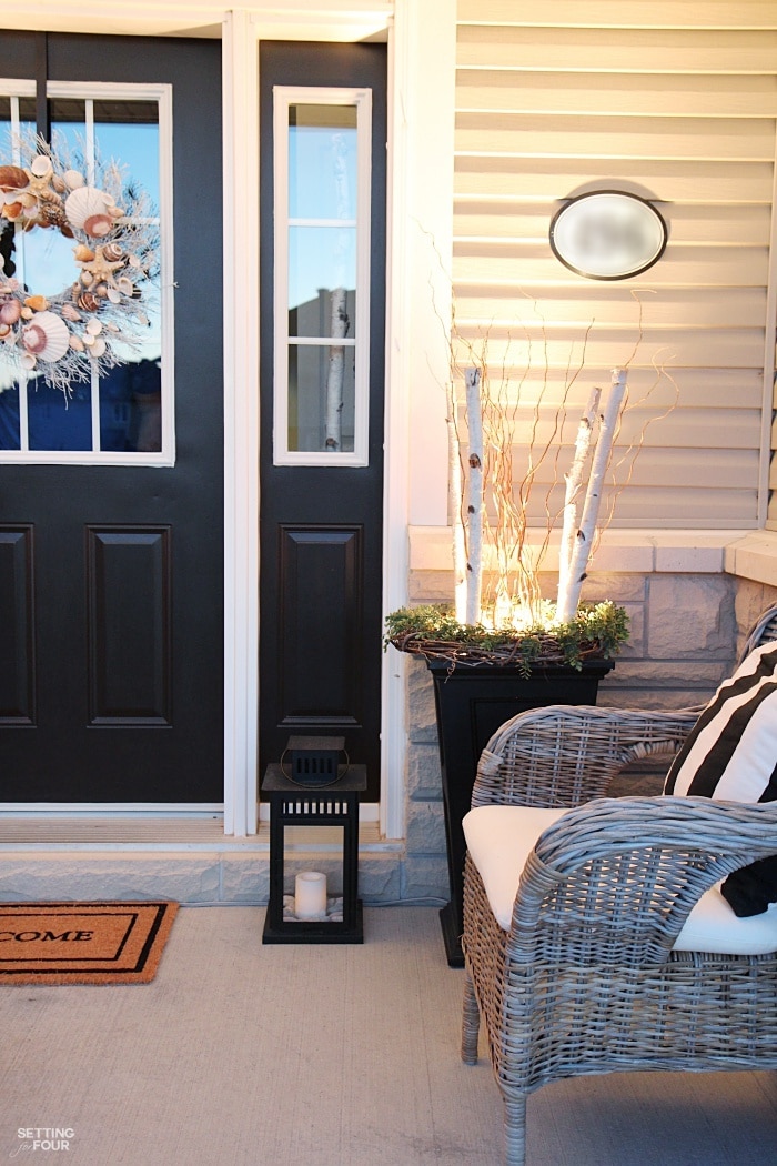 Front porch decorated with lights in urns at night.