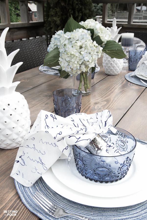 Summer outdoor dining. Table setting in blue and white. Hydrangea centerpiece, white ceramic pineapple decor.