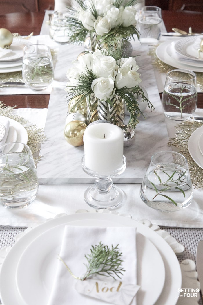 Learn how to create this Elegant Gold And White Christmas Tablescape that's quick and easy to put together! Give white dishes a festive look with white, silver and gold Christmas ball ornaments and beautiful DIY white rose and pine winter centerpieces. This Christmas table decor is perfect for holiday dinner with the family, big dinner parties and winter weddings too!