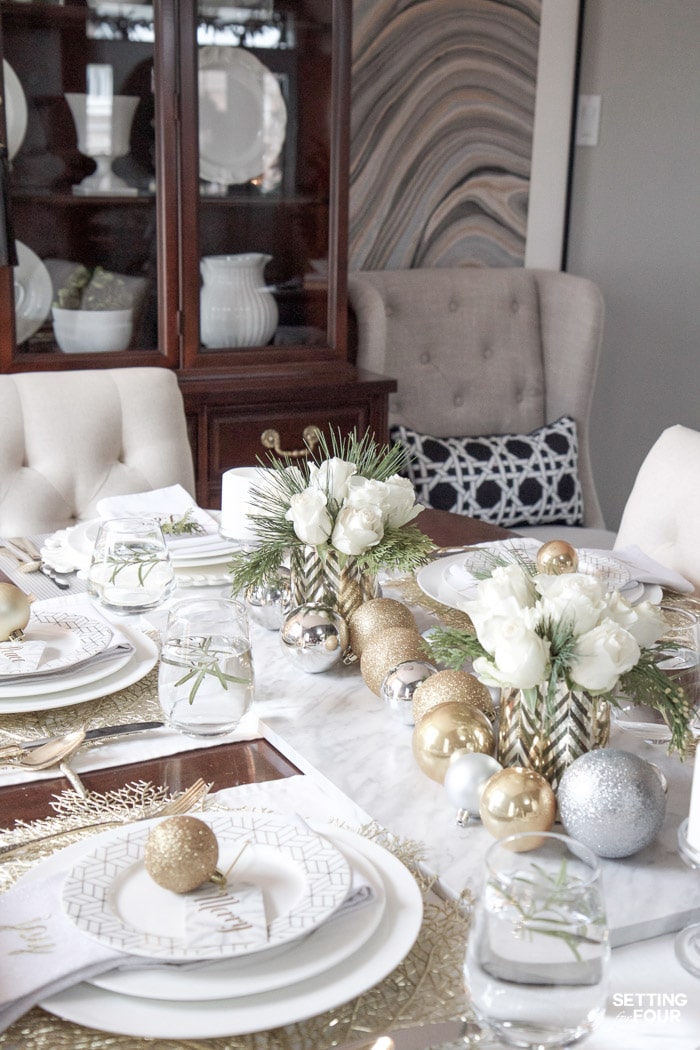 Learn how to create this Elegant Gold And White Christmas Tablescape that's quick and easy to put together! Give white dishes a festive look with white, silver and gold Christmas ball ornaments and beautiful DIY white rose and pine winter centerpieces. This Christmas table decor is perfect for holiday dinner with the family, big dinner parties and winter weddings too!