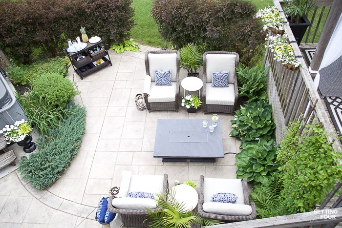 Patio seating area with outdoor furniture, bar cart, fire table, container flowers and landscaped back yard.