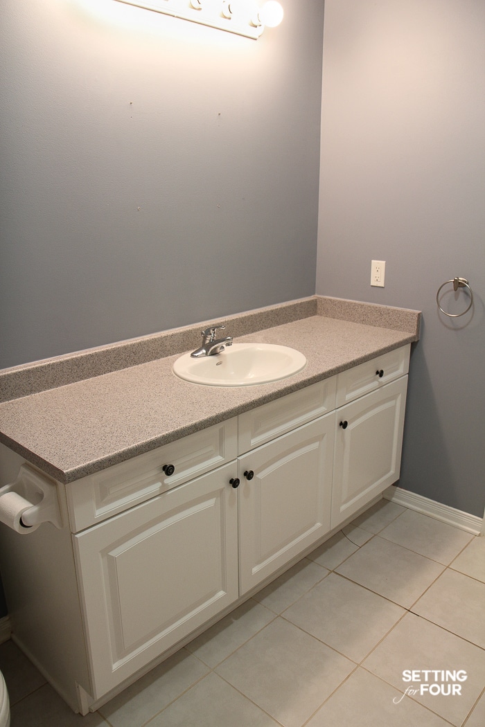 Dark bathroom with white vanity cabinet and Hollywood vanity lights. Cracked floor tile.