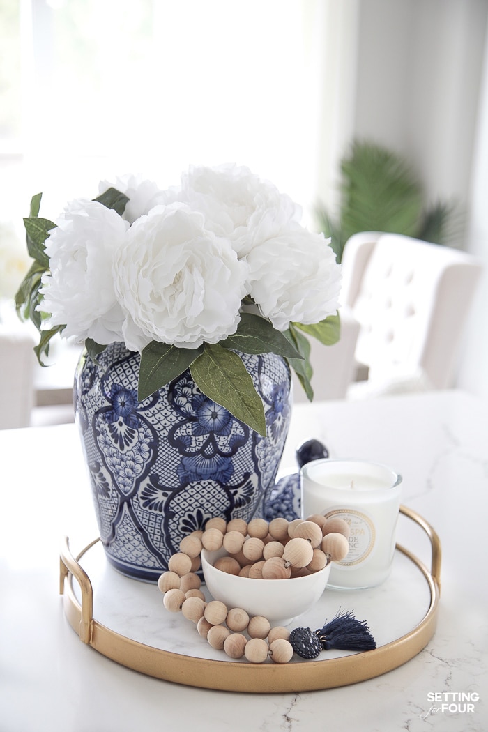 Gold and marble tray decorated with a blue and white ginger jar in a chinoiserie pattern filled with white peonies and Wood bead garland and a white candle.