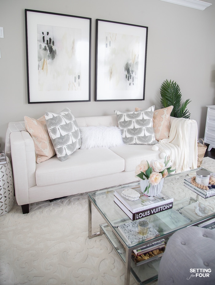 A cozy living room with large wall art, pillows on beige sofa, tiered coffee table and ivory rug.