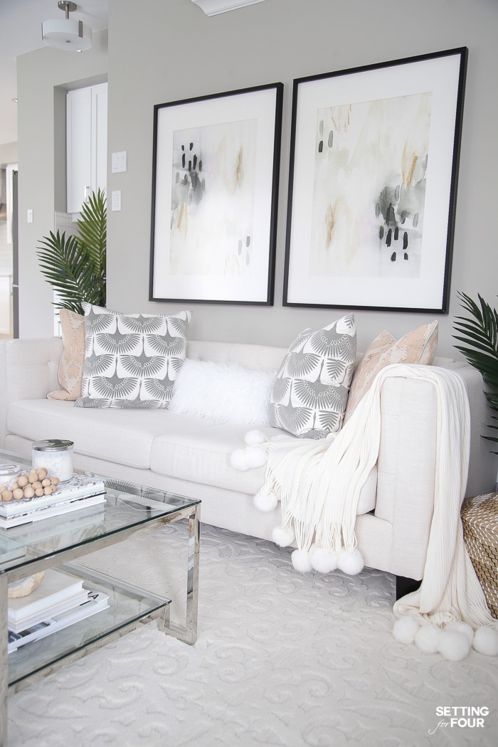 Gray living room walls, black framed prints, beige sofa, pink and gray pillows and pom pom throw blanket