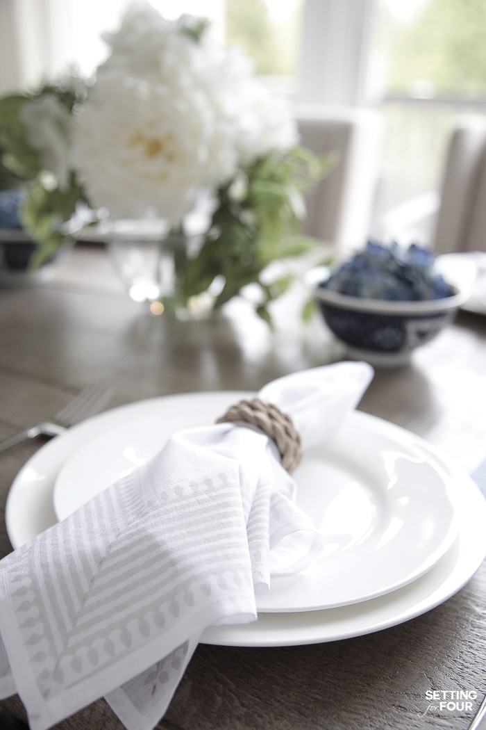 Summer tablescape with white dinnerware, gray striped napkins, rope napkin ring and blue and white bowls filled with blue hydrangeas.