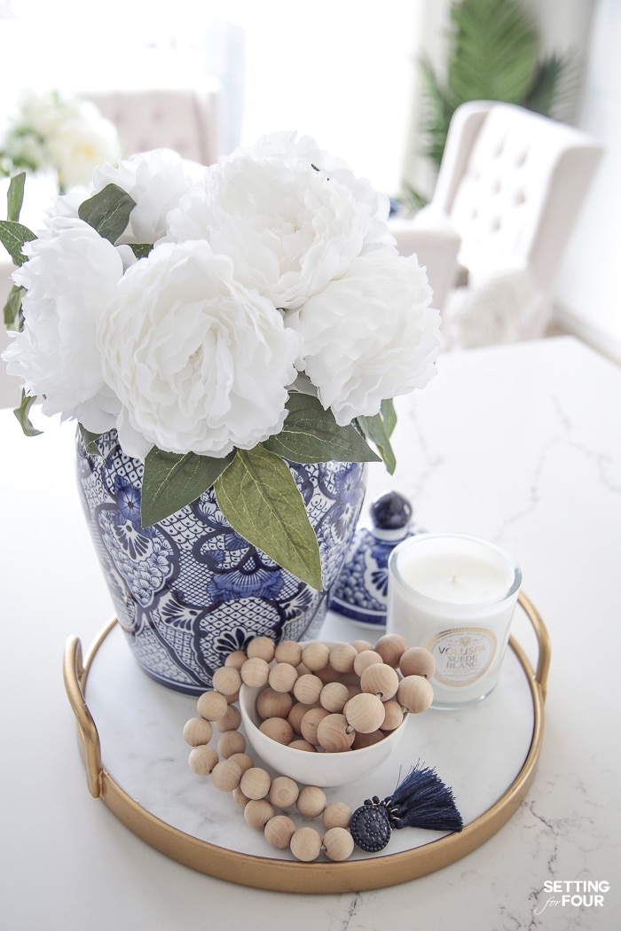 Gold tray on a kitchen island. Chinoiserie ginger jar filled with white flowers. Farmhouse wood bead garland decor and White candle.