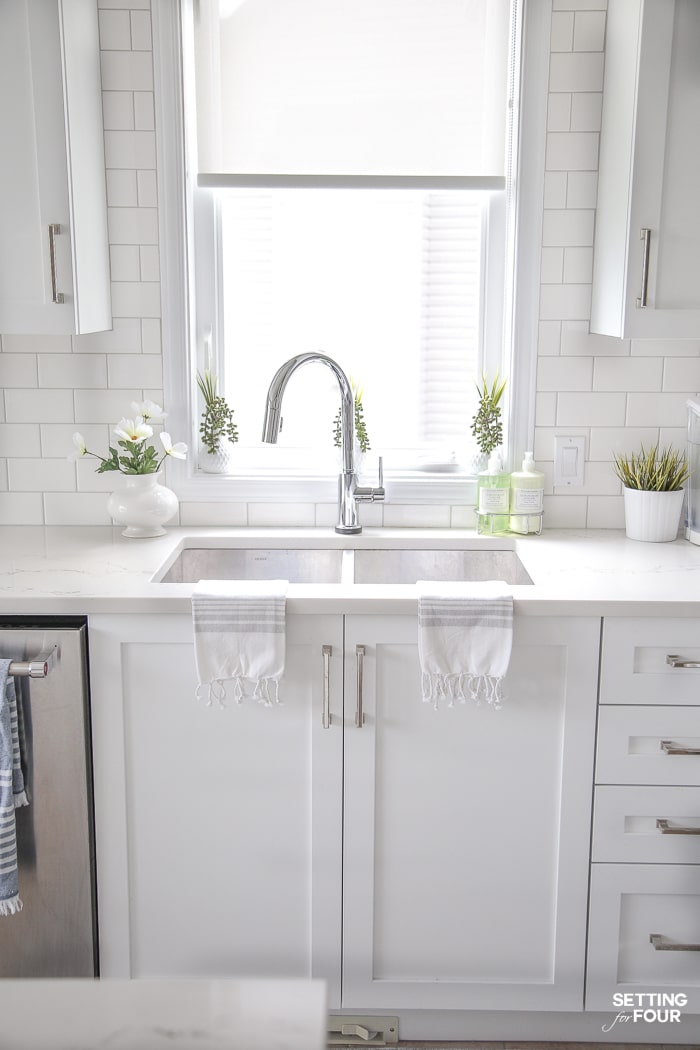 Kitchen window decorated with white vases filled with string of pearls succulents and decorative grass. 