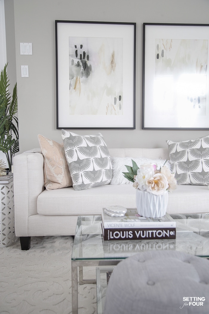 Modern living room decorations. Tuxedo sofa, glass coffee table, gray poufs and large wall art.