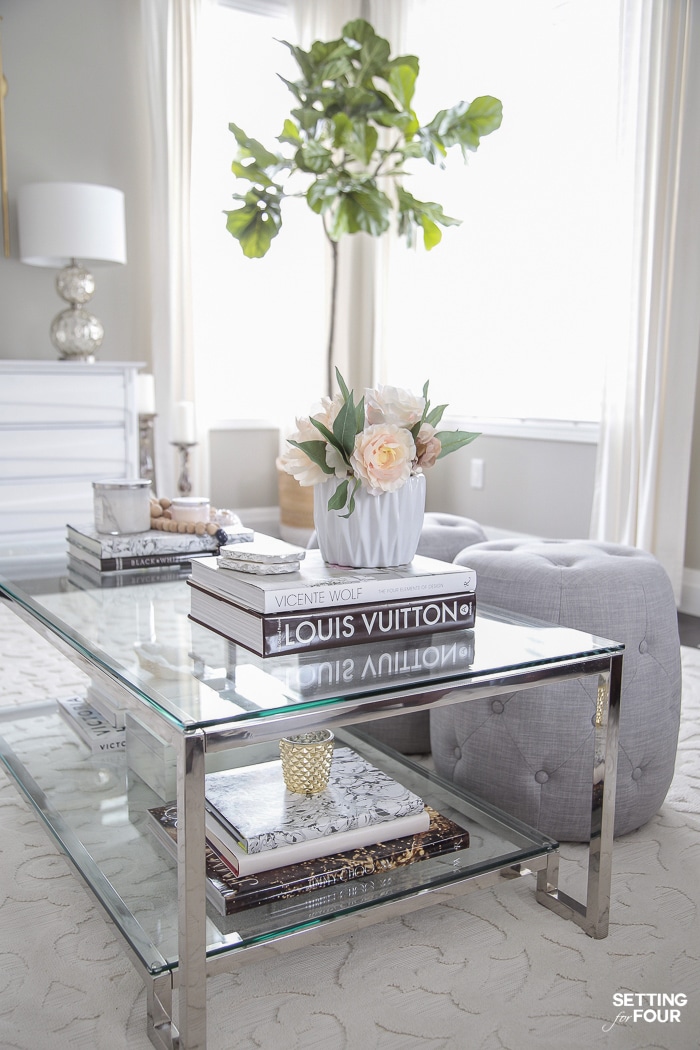 Traditional living room decor with glass coffee table, gray walls, gray poufs and fiddle leaf fig tree.