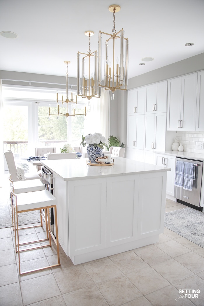 White kitchen decorated for summer with blue accents and brass and crystal pendants over kitchen island.