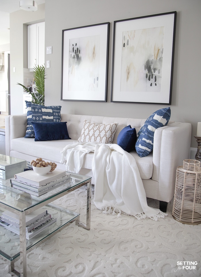 Coastal style living room with two large abstract art pieces hung above the sofa. Blue and white pillows.