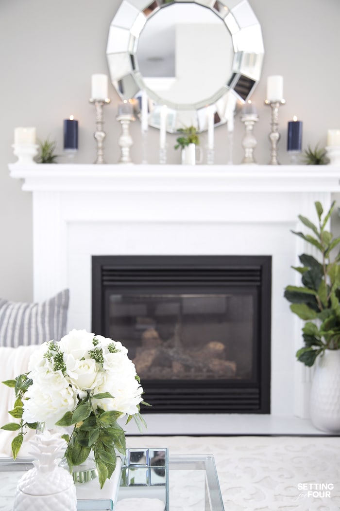 White painted fireplace tile and mantel. Large round mirror over mantel. Summer decor. Candles and air plants on mantel.