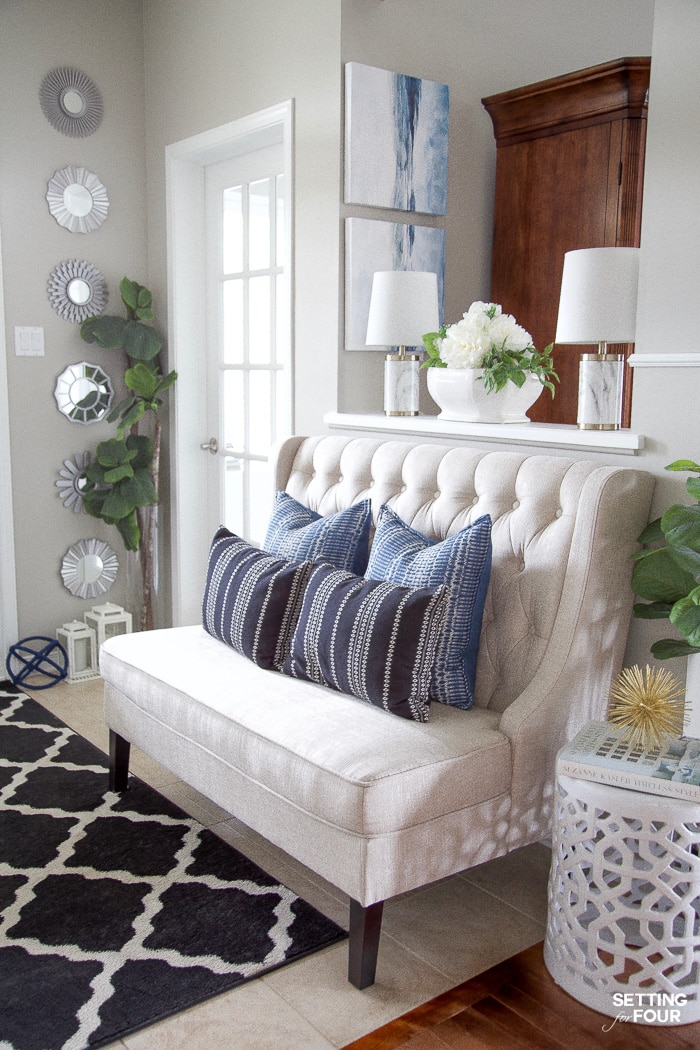 Entryway with bench, black trellis rug, blue and black pillows, coastal art and white garden stool