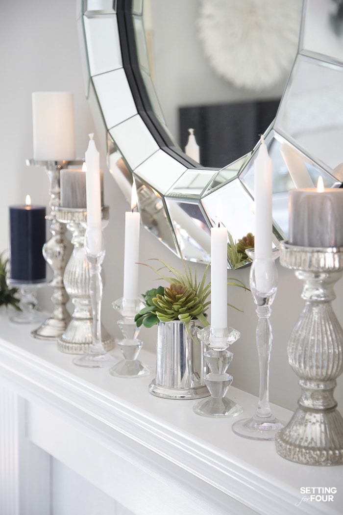 Round mirror hung over white fireplace mantel with candlesticks and candles.