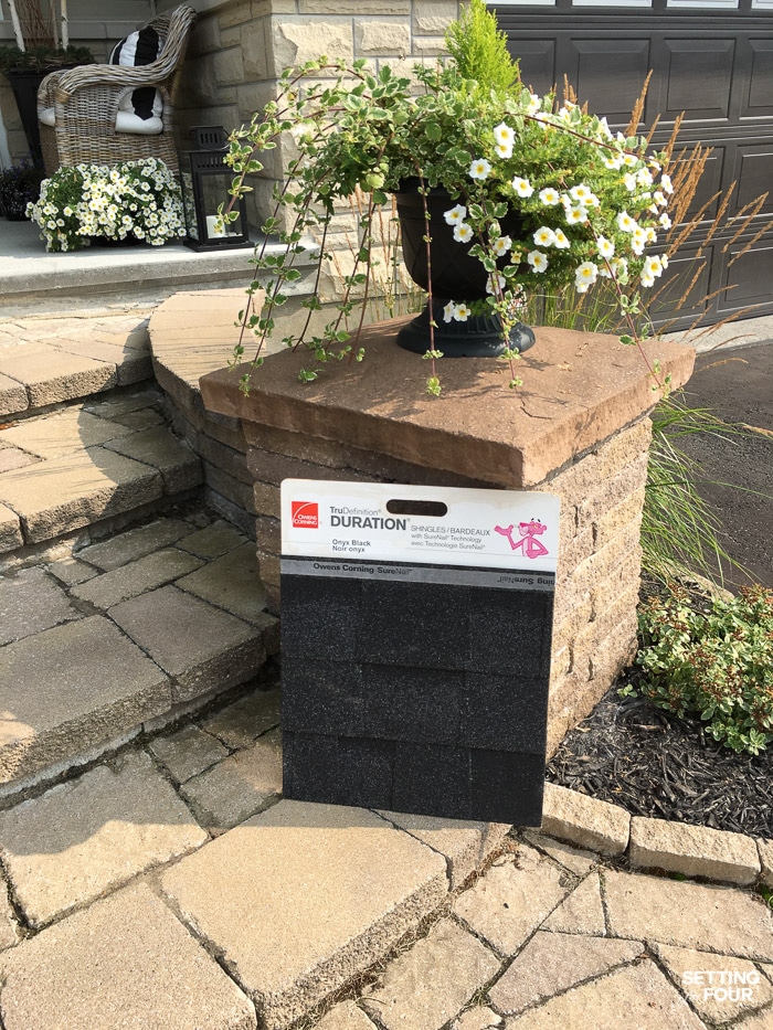 Shingle sample propped up onto a brick pillar and interlock walkway of a home.