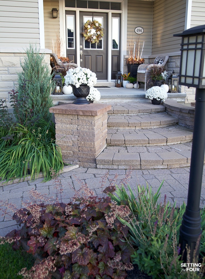 Front of house with stone steps. Decorated for fall with mums and a wreath. Flower bed with heuchera plants.