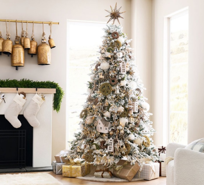 An artificial flocked Christmas tree with white and gold ornaments in a white living room with a fireplace.