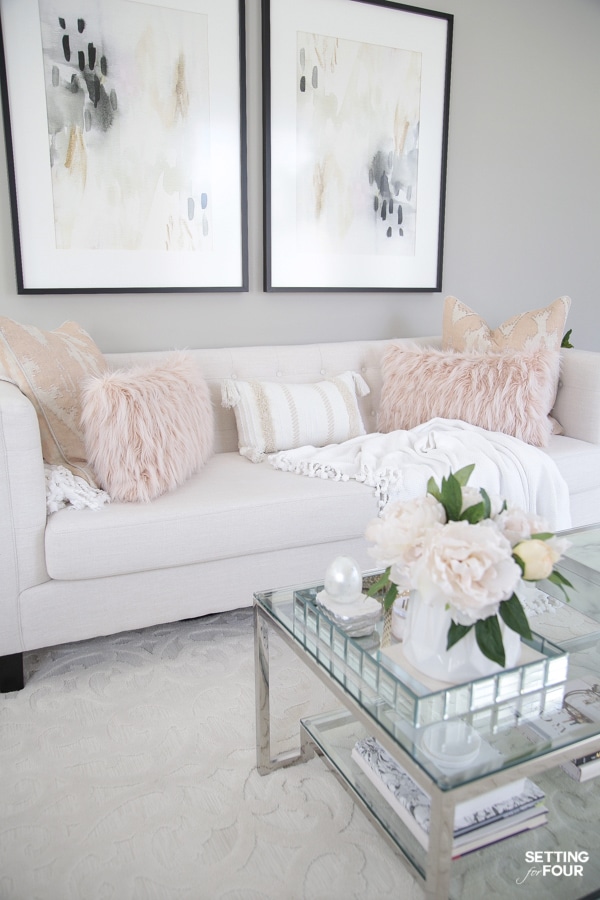 White sofa with blush pink pillows and wall art in living room