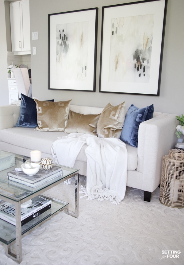 Living room sofa with greek key pillows in gold and blue, abstract wall art and glam coffee table.