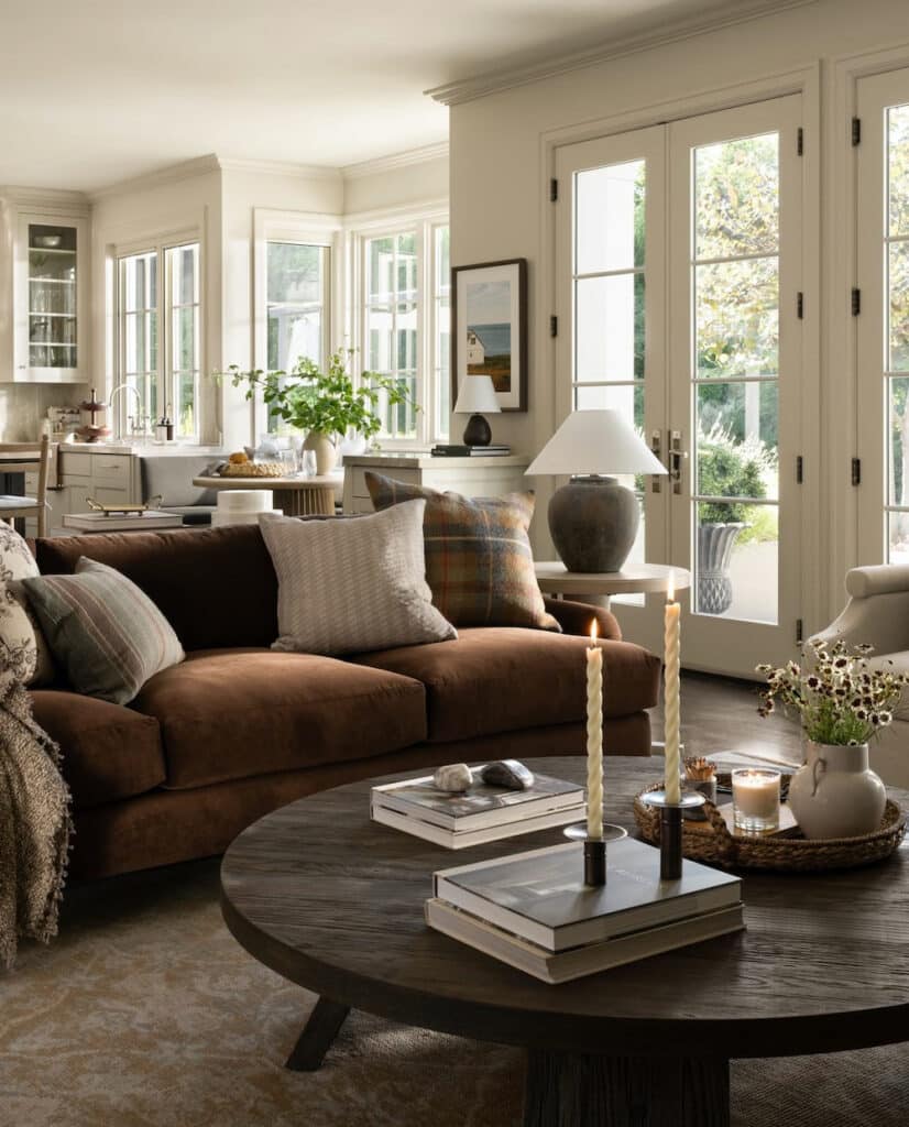 Cozy, Neutral Living Room Decorating Ideas, brown sofa with brown wood round coffee table decor ideas and open concept layout with kitchen and dining nook, cohesive style and texture, vintage decor, rustic modern design, cream colored walls.