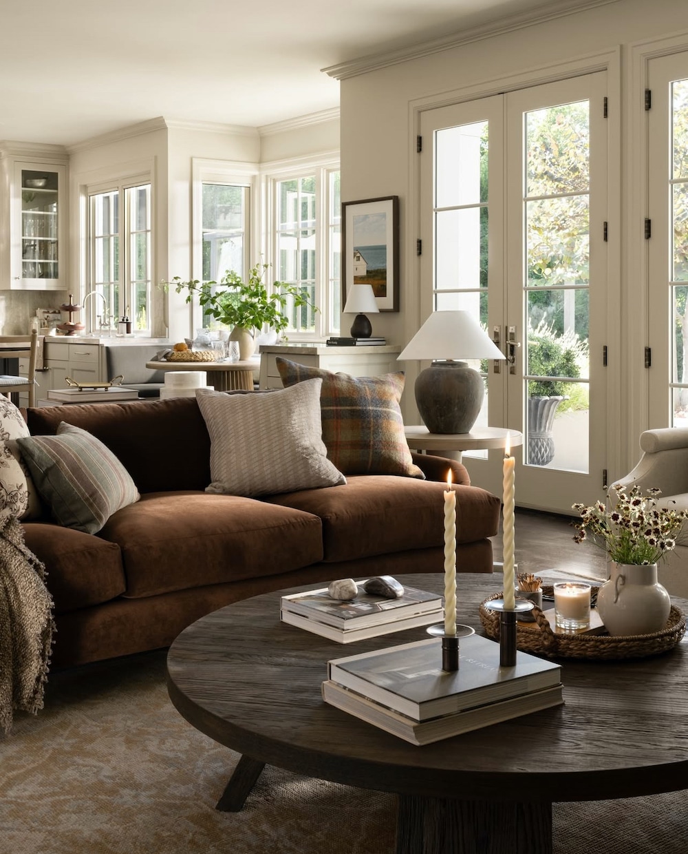 Furniture Placement Living Room Ideas In An Open Concept Home, earthy brown sofa with round wood coffee table, coffee table decor ideas, open to the breakfast nook and kitchen, modern, minimalist, transitional, amber interiors style, cozy, elegant, warm color palette, earth tones color scheme, 2025 design trends, black, white walls french doors in living room
