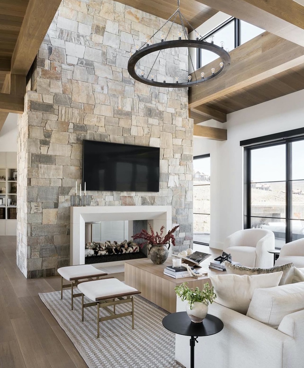 How To Arrange Furniture In An Open Concept Layout - Living Room With TV ideas, tv above plaster fireplace surround and natural stone wall, black chandelier for a living room, ottoman stools for balance, sofa and 2 chairs, square coffee table decor ideas, neutral color palette, white walls, wood vaulted ceiling, black windows, white sofa idea, organic modern, transitional, mountain home, rustic, luxury, minimalist, Studio McGee, Pottery Barn style