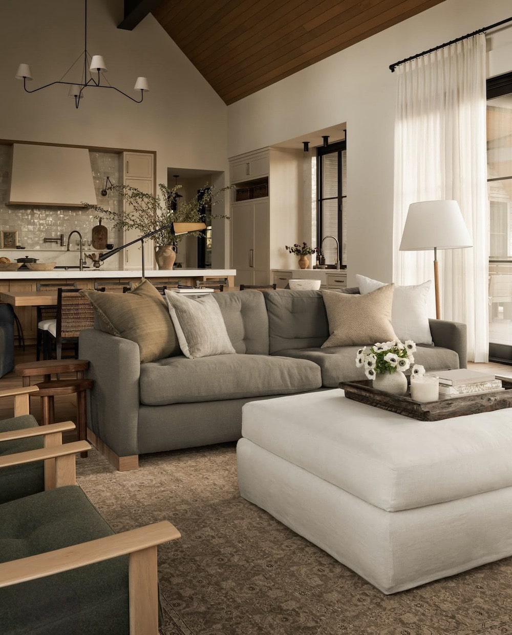 Moody, Earthy Living Room Layout With 2 Sofas and 2 Chairs Furniture Arrangement Idea, upholstered coffee table ottoman with tray, gray sofa with earth tone pillows, living room open to kitchen, sofa and 2 chairs layout, cozy, elegant, organic modern, minimalist, transitional, farmhouse interior, new home build inspo