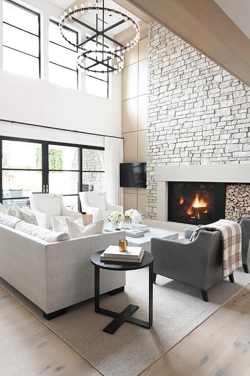 Living Room Furniture Arrangement With A Sofa and 2 Chairs Layout Ideas, black Restoration Hardware style living room chandelier, natural stone fireplace, cozy, TV beside fireplace, gray chairs, white sofa, beige, light wood floors, white walls, black windows, how high to hang curtains above sliders glass doors, light wood beams, modern, transitional, minimalist, new home ideas, McGee