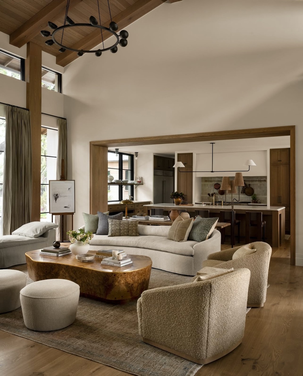 Open Concept Furniture Layout Idea For A Living Room and Kitchen, cohesive, flow, sofa with 2 chairs, bench, coffee table and 2 ottomans, modern black chandelier, wood ceiling, wood trim, moody, earthy, cozy, warm colors, white, beige, brown, black, linear pendant over kitchen island, Pottery Barn style, Crate and Barrel Style, McGee 