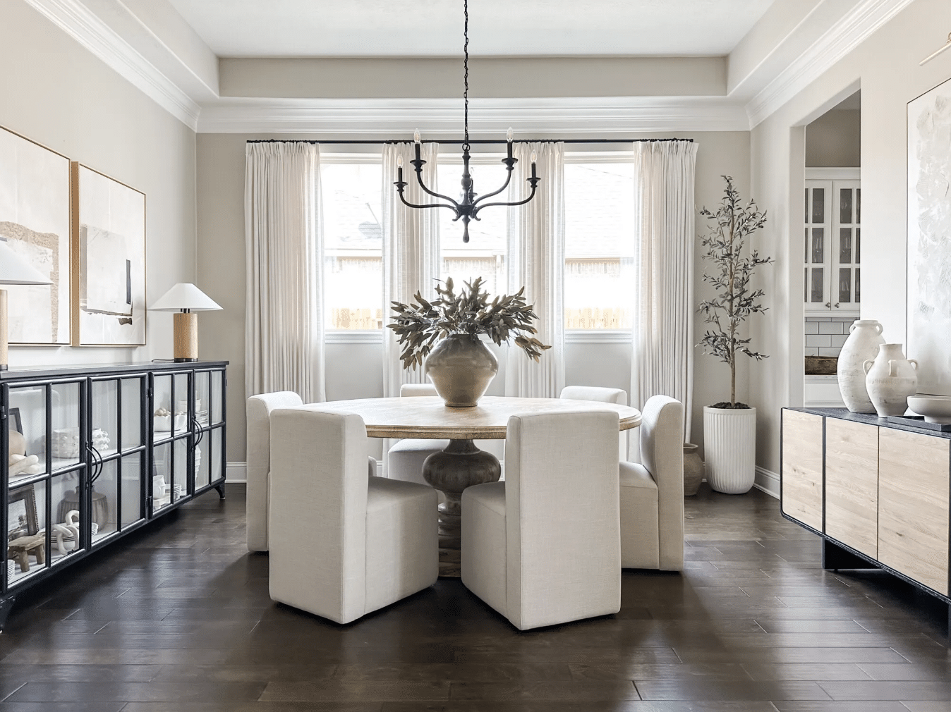 Sherwin Williams Repose Gray Dining Room Paint Color Inspiration, warm, griege, round dining table with upholstered chairs on castor wheels, black chandelier, black sideboard cabinet, white curtains, black curtain rod, simple greenery arrangement in vase, organic modern, transitional, dark brown wood floors