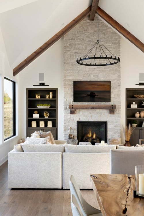 Modern Transitional Living Room Open Concept Layout With TV Above Fireplace Idea, sectional sofa facing fireplace, natural stone fireplace, round black chandelier in vaulted ceiling with beams, builtin bookcases, rustic wood mantel, minimalist, farmhouse, new home ideas, living room remodel
