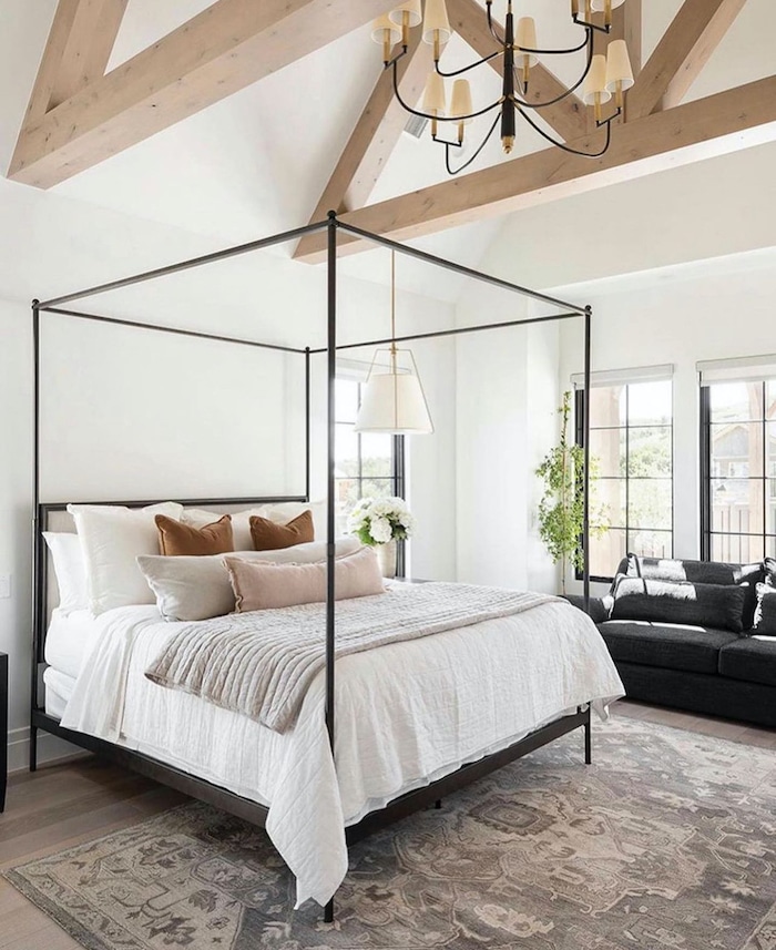Love this beautiful neutral bedroom design with beams and canopy bed. Sofa sitting area in bedroom. Bright, airy white walls in bedroom. Bedroom chandelier. Organic modern, farmhouse, transitional design.