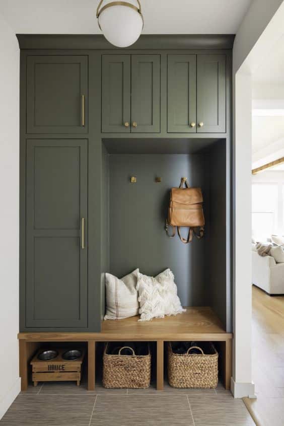 Small Entryway Built In Storage Ideas. Green colored built in cabinets with bench and baskets for shoe storage and dog bowl. Hooks hang baskets. Locker and upper cabinets for extra storage.