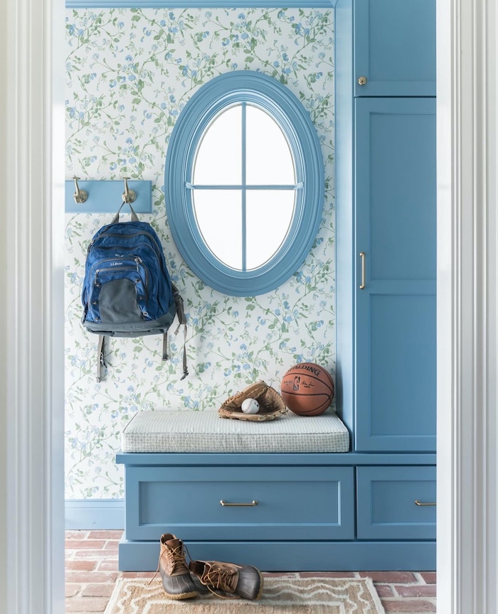 Beautiful Wall Mounted Coat Rack & Built In Cabinet For Backpack Storage. Blue cabinets. Oval Window. Floral Wallpaper. Small mudroom bench with storage. 