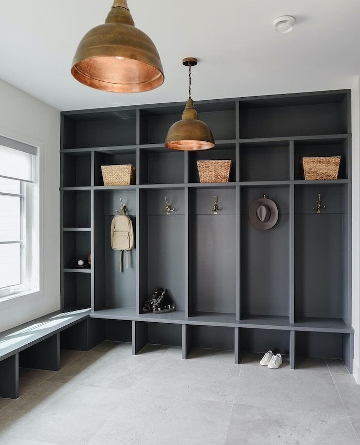 Mudroom built in cabinets use vertical wall space to organize backpacks, shoes and hats.  Modern mudroom storage ideas with open shelves, bench, cubby compartments. Black mudroom cabinets.