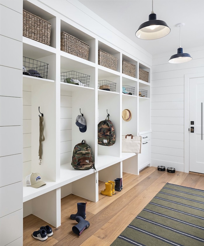 Bright, organized mudroom storage ideas with bench, cubbies, baskets, hooks for hats, backpacks and bags, and neatly placed shoes and boots on a wooden floor. Cozy and functional.
