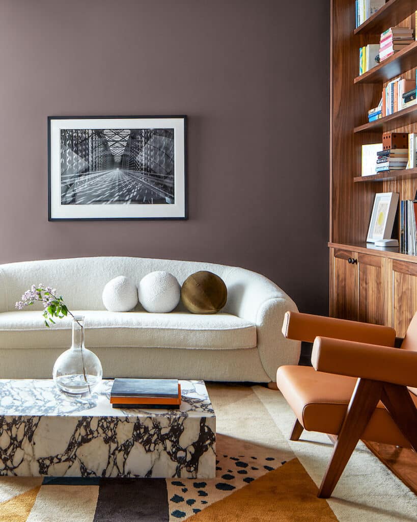 Benjamin Moore Cinnamon Slate Modern Living Room Paint Color Idea. boucle curved sofa, bookcase, marble coffee table, plum purple color palette, color of the year 2025, plum, brown, cozy, elegant, wall color, painting inspiration, 2025 design trends.