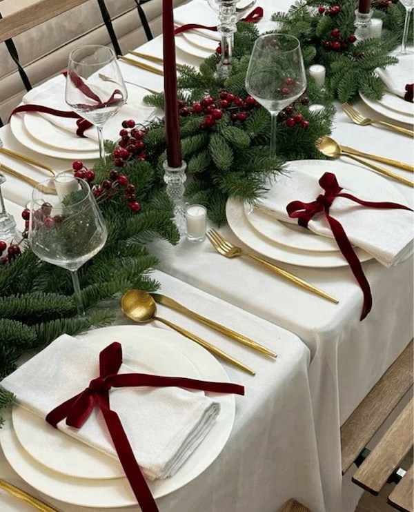 Elegant White and Red Christmas Table Decoration Ideas. These beautiful red velvet bows and white napkins look so classy with the green garland and gold flatware.