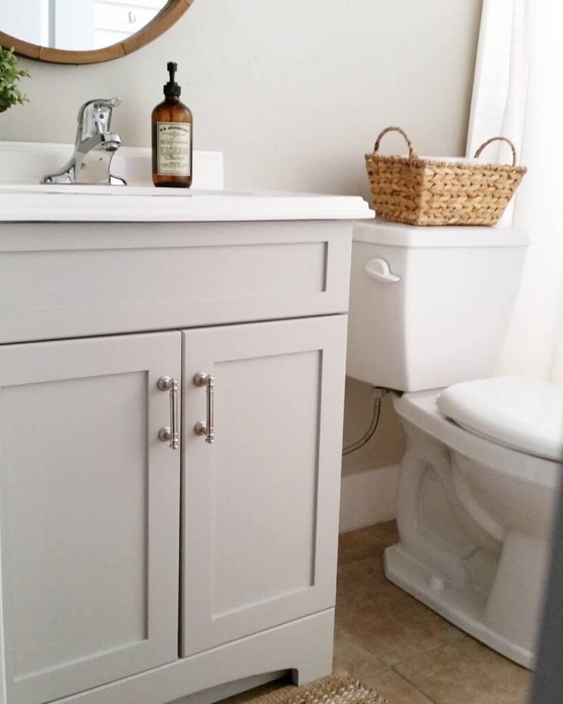 Sherwin-Williams Repose Gray bathroom vanity cabinet with white countertop, silver hardware, warm neutral walls, and white bathroom fixtures