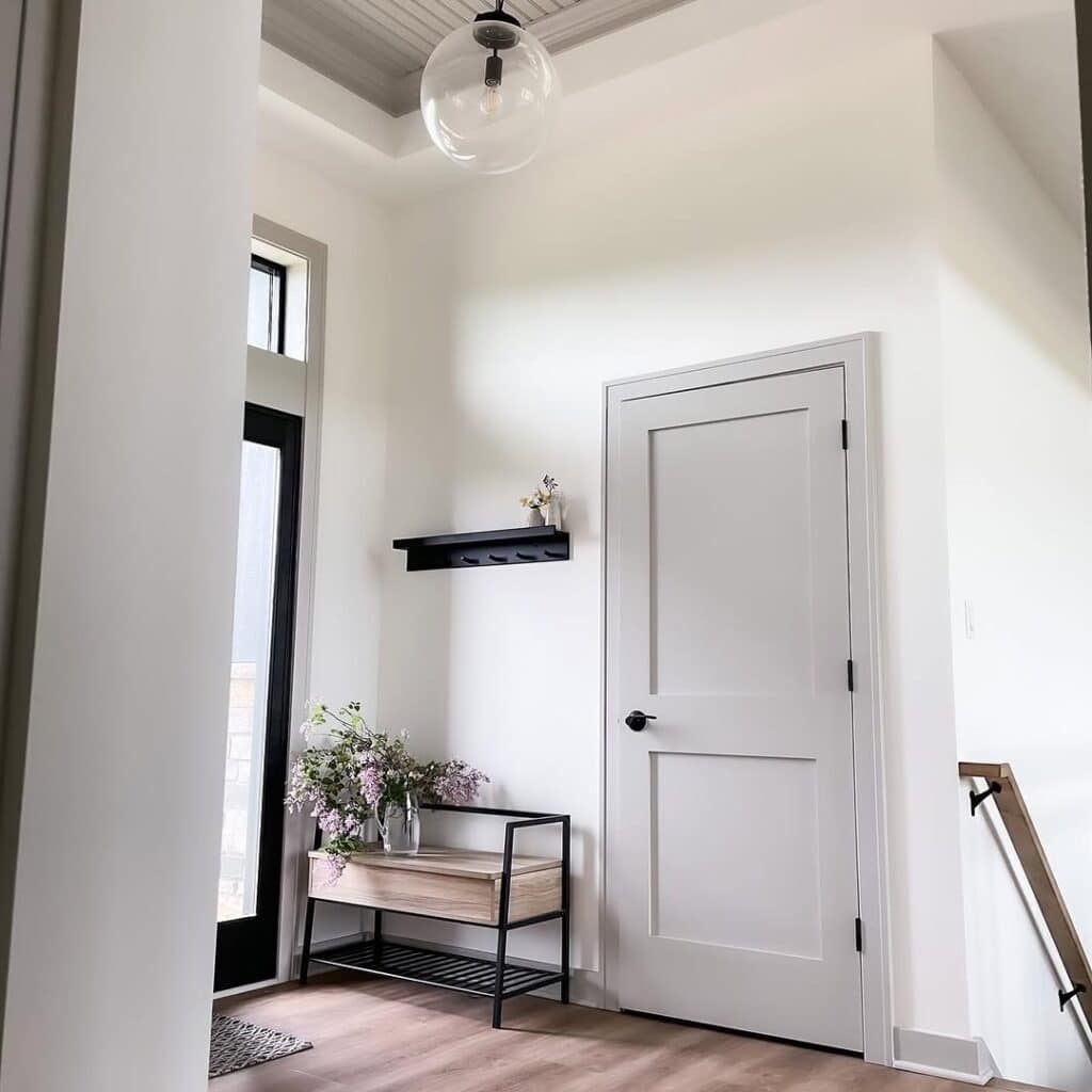 Sherwin-Williams Repose Gray interior door and trim in an entryway with white walls, black accents, warm wood flooring, and modern bench