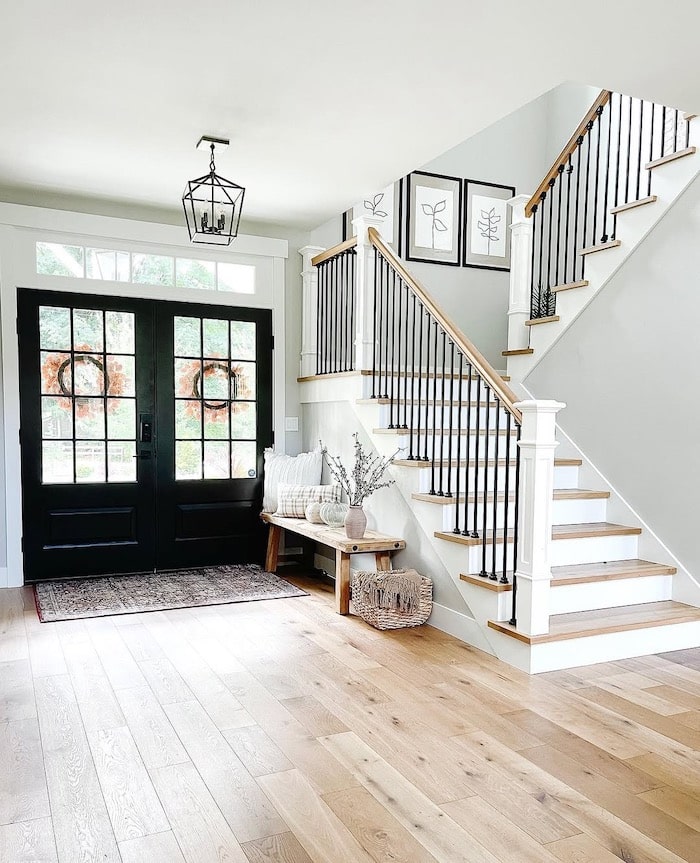 Sherwin-Williams Repose Gray entryway with white trim, black double front doors, light wood floors, and staircase with black balusters and wood handrail