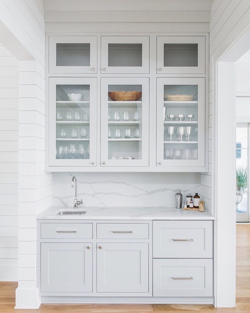 Sherwin-Williams Repose Gray pantry cabinets with glass-front doors, white shiplap walls, white countertops, and light wood flooring