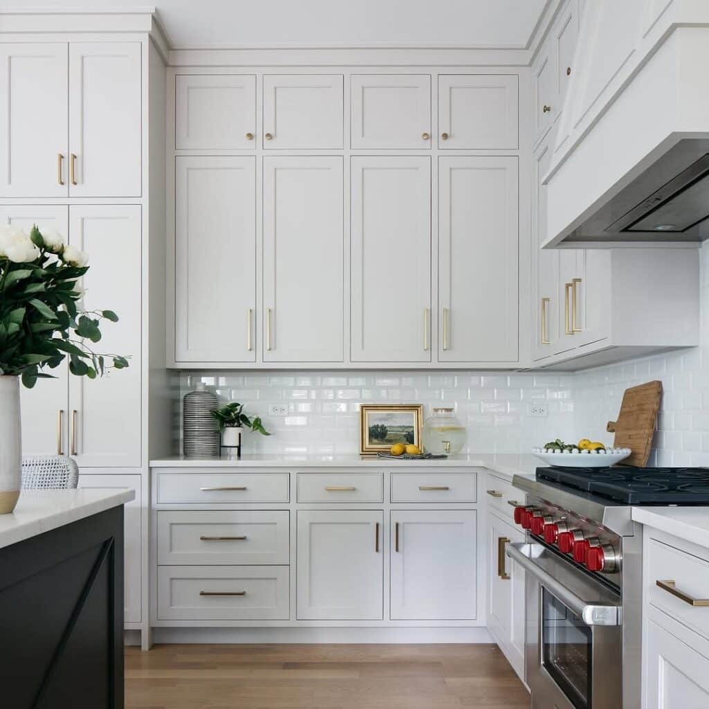 Sherwin-Williams Repose Gray kitchen cabinets with white countertops, white subway tile backsplash, brass hardware, stainless steel range, and warm wood flooring