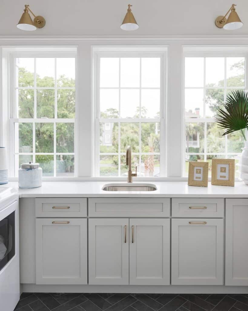 Sherwin-Williams Repose Gray kitchen cabinets with white countertops, brass hardware, large windows, and black tile flooring