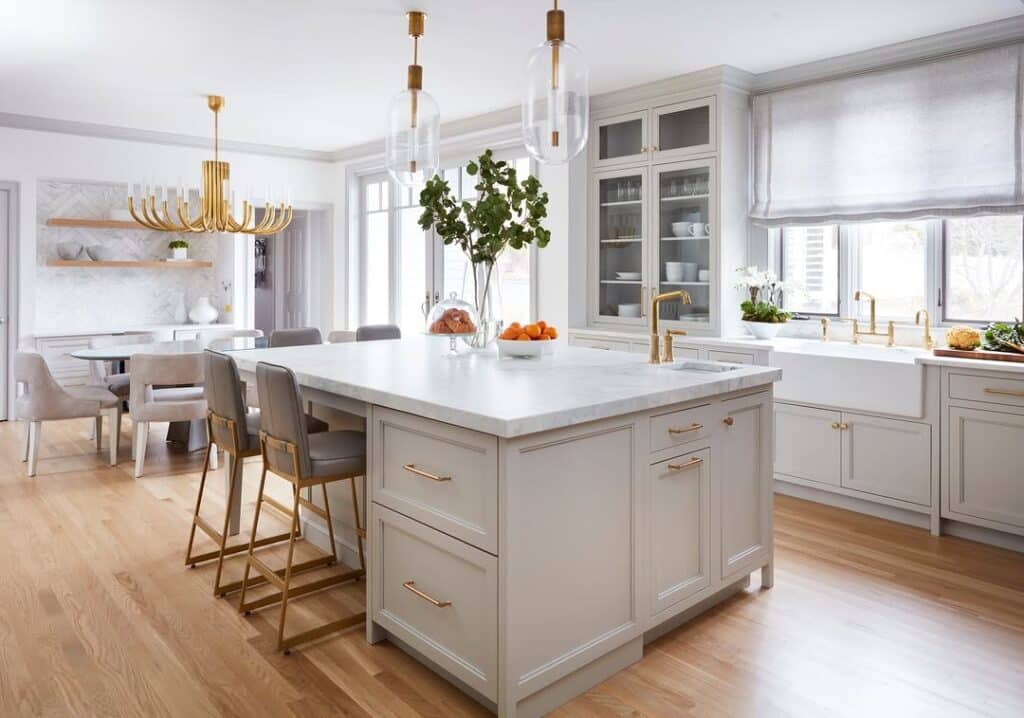 Sherwin-Williams Repose Gray kitchen cabinets with white countertops, large island, brass hardware, warm wood flooring, pendant lighting, and dining area