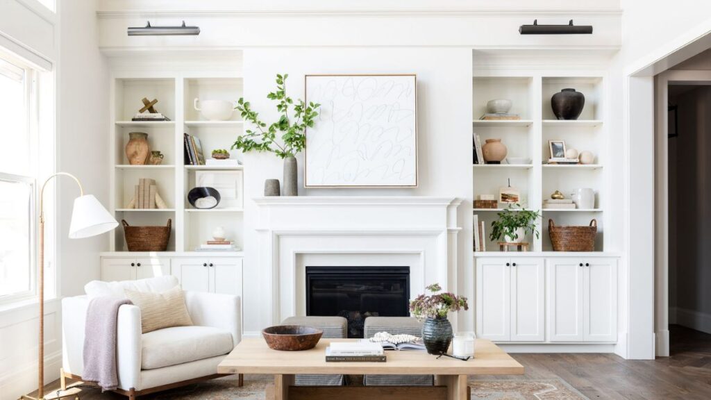 Bright neutral living room with a white fireplace mantel, built-in shelves, cozy accent chair, wood coffee table, and organic modern decor showing how to arrange living room furniture with a fireplace.